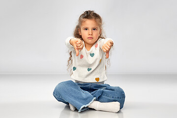 Image showing sad girl sitting on floor and showing thumbs down