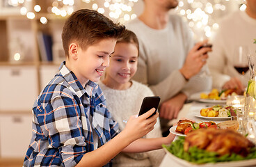 Image showing boy with sister using smartphone at family dinner