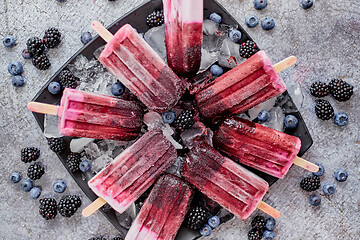 Image showing Homemade fresh frozen blueberry and blackberry popsicles on black plate with ice sitting on stone