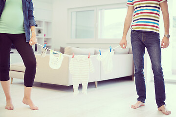 Image showing young couple holding baby bodysuits at home