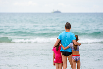 Image showing Dad with two daughters are hugging on the seashore and looking into the distance