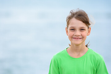 Image showing Portrait of a happy ten-year-old girl in a green t-shirt on the background of the sea