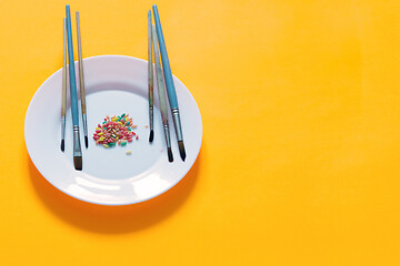 Image showing Brushes and rice painted in different colors on a plate, yellow background