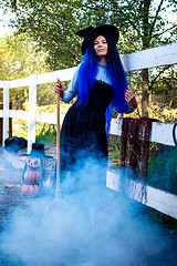 Image showing A girl dressed as a witch stands at a fence on a farm, smoke from below, pumpkins in the background