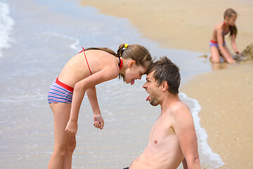 Image showing Dad and daughter butt heads while sitting on the sea sandy shore