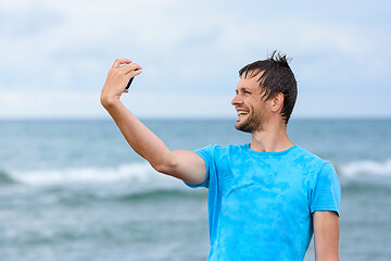 Image showing A man on vacation takes pictures of himself on a mobile phone