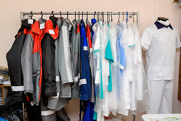 Image showing Sewn clothes hang on a large pipe hanger in a sewing workshop