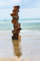 Image showing A tower made of wet pieces of wood stands on the wave-laden seashore