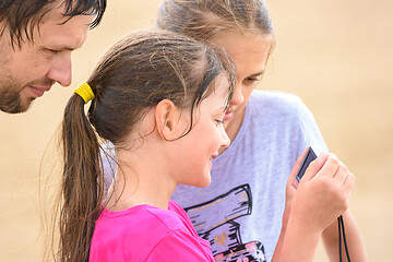 Image showing Two girls and dad are looking at photos on the camera from a family beach vacation