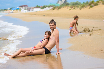 Image showing Dad and daughter are sitting in the foreground, in the background a girl is building a sand castle