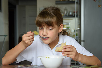 Image showing Girl at home eating soup from a white bowl at the dinner table