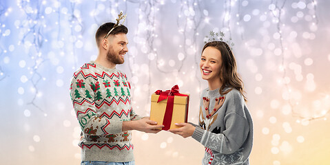 Image showing happy couple in ugly sweaters with christmas gift