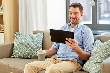 Image showing smiling man with tablet pc drinking coffee at home