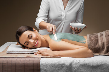 Image showing woman and cosmetologist applying clay mask in spa