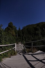 Image showing wooden old bridge in forest over treetops in night with stars