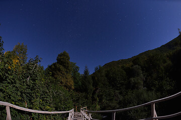 Image showing wooden old bridge in forest over treetops in night with stars