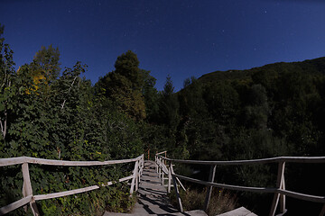 Image showing wooden old bridge in forest over treetops in night with stars