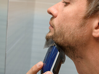 Image showing A man cuts a regrown beard on his chin using a hair clipper