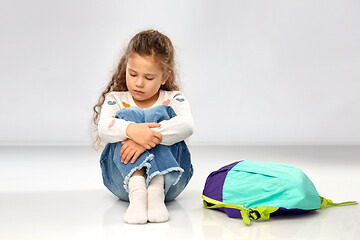 Image showing sad little girl with school bag sitting on floor