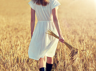 Image showing young woman with cereal spikelets walking on field