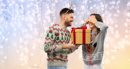 Image showing happy couple in ugly sweaters with christmas gift