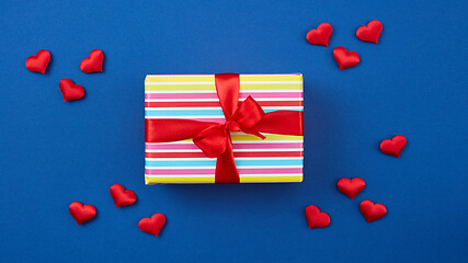 Image showing wrapped gift box with red ribbon and hearts on blue background