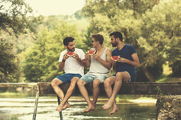 Image showing men enjoying watermelon while sitting on the wooden bridge