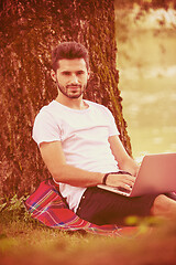 Image showing man using a laptop computer on the bank of the river