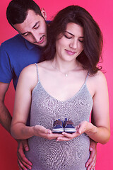 Image showing young pregnant couple holding newborn baby shoes