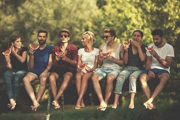 Image showing friends enjoying watermelon while sitting on the wooden bridge