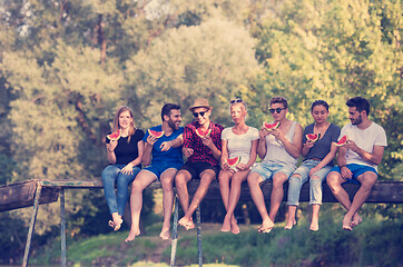 Image showing friends enjoying watermelon while sitting on the wooden bridge