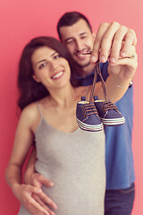 Image showing young pregnant couple holding newborn baby shoes