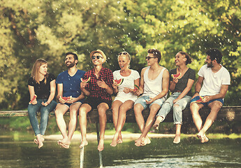 Image showing friends enjoying watermelon while sitting on the wooden bridge