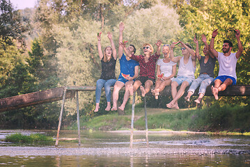 Image showing friends enjoying watermelon while sitting on the wooden bridge