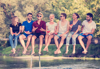 Image showing friends enjoying watermelon while sitting on the wooden bridge