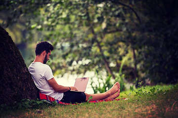 Image showing man using a laptop computer on the bank of the river