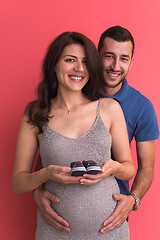 Image showing young pregnant couple holding newborn baby shoes