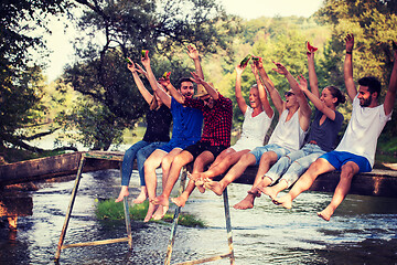 Image showing friends enjoying watermelon while sitting on the wooden bridge