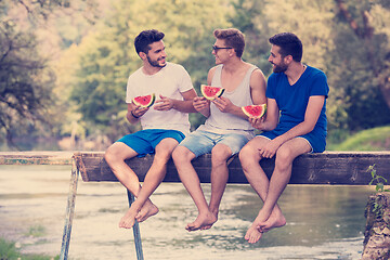 Image showing men enjoying watermelon while sitting on the wooden bridge