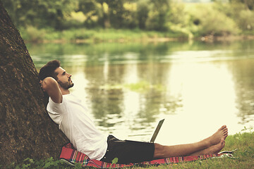 Image showing man using a laptop computer on the bank of the river