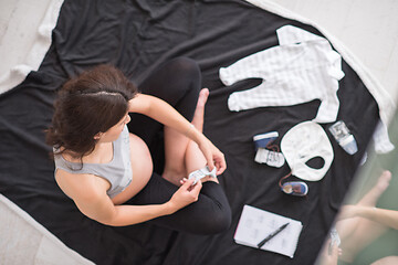 Image showing top view of pregnant woman checking list of baby clothes