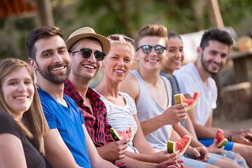 Image showing friends enjoying watermelon while sitting on the wooden bridge