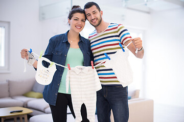 Image showing young couple holding baby bodysuits at home
