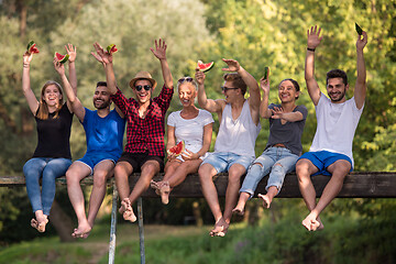 Image showing friends enjoying watermelon while sitting on the wooden bridge