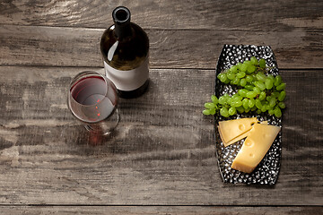 Image showing A bottle and a glass of red wine with fruits over wooden background