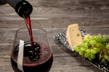 Image showing A bottle and a glass of red wine with fruits over wooden background