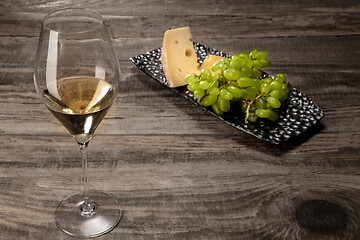 Image showing A bottle and a glass of white wine with fruits over wooden background