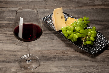 Image showing A bottle and a glass of red wine with fruits over wooden background