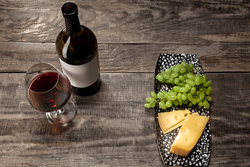 Image showing A bottle and a glass of red wine with fruits over wooden background