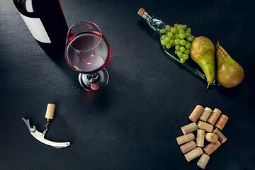 Image showing A bottle and a glass of red wine with fruits over dark stone background